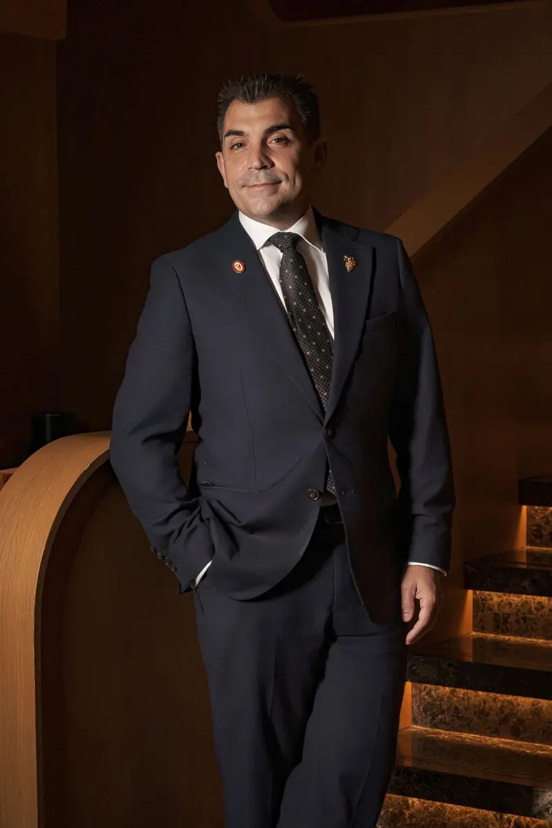 Sommelier in a navy suit and tie standing by a staircase